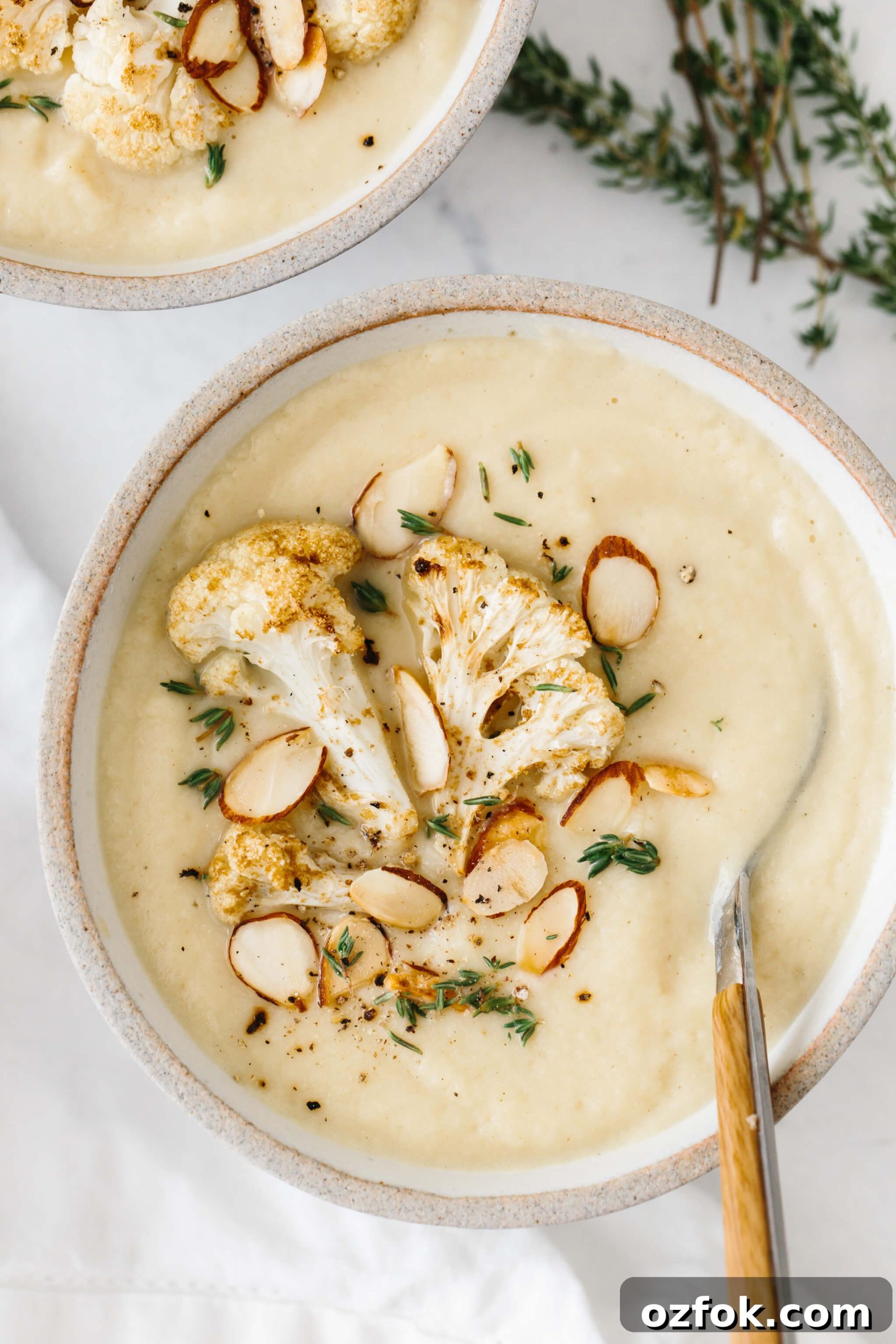 Roasted Cauliflower soup in a bowl, topped with cauliflower, almonds and thyme.