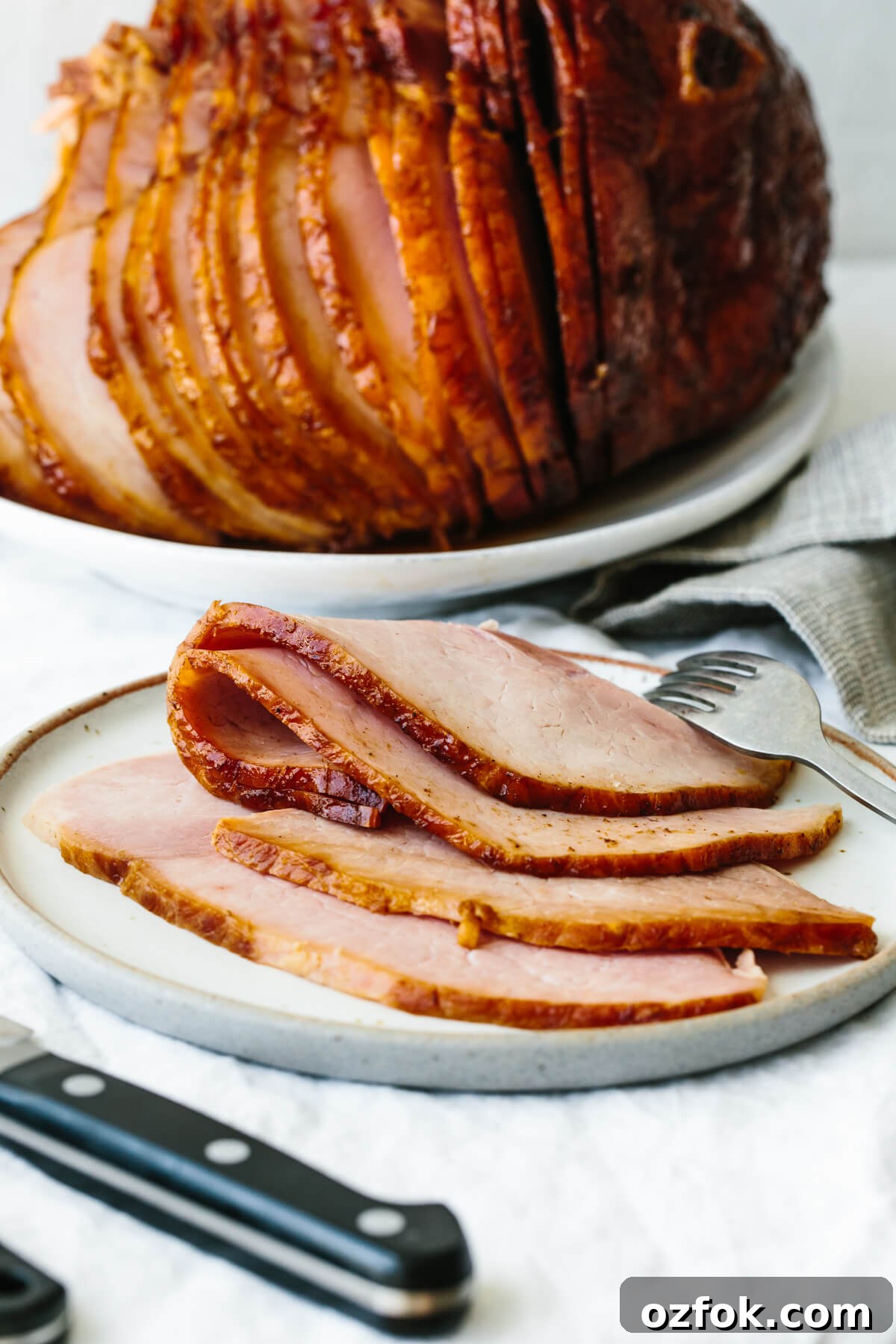 Sliced honey baked ham on a plate with a fork