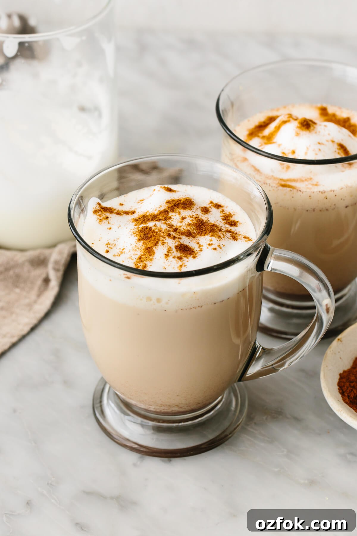 2 mugs of chai latte next to a milk frother.