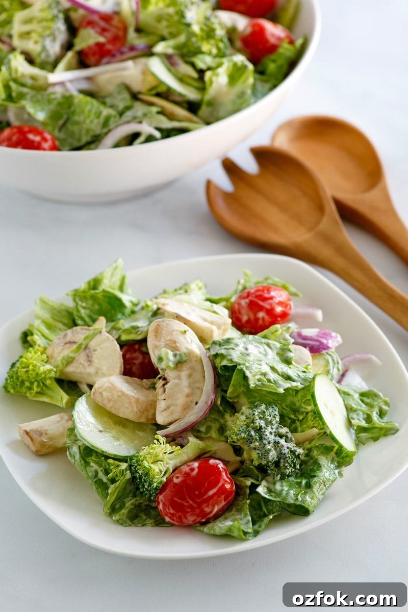 White bowl of Romaine and Broccoli Salad with a white plate of salad on the side