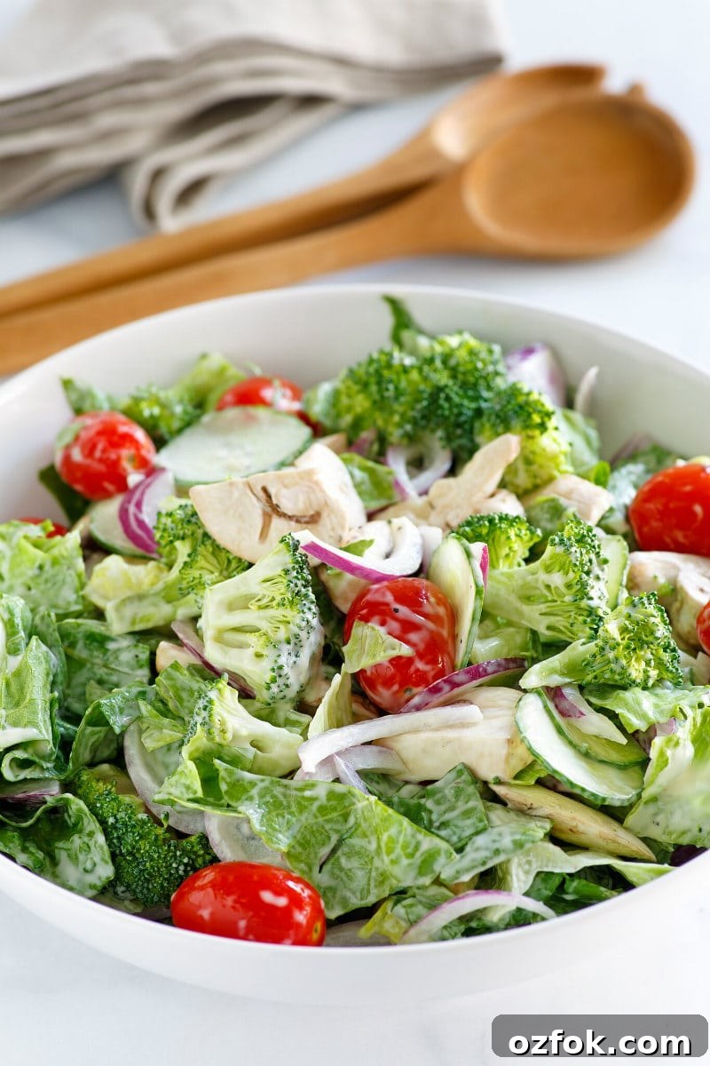 White bowl of Romaine and Broccoli Salad with wooden serving utensils in the background