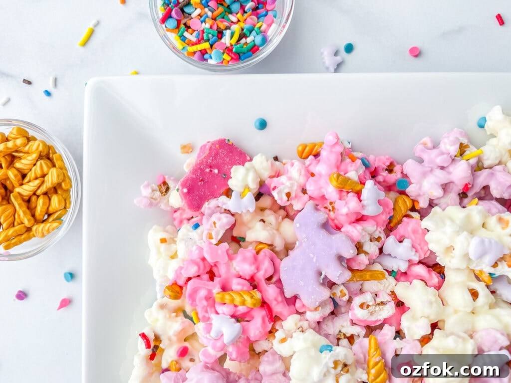 Unicorn Popcorn Recipe for a Magical Party Treat 3 A close up of candy coated popcorn, topped with purple cookies and sprinkles in the background.
