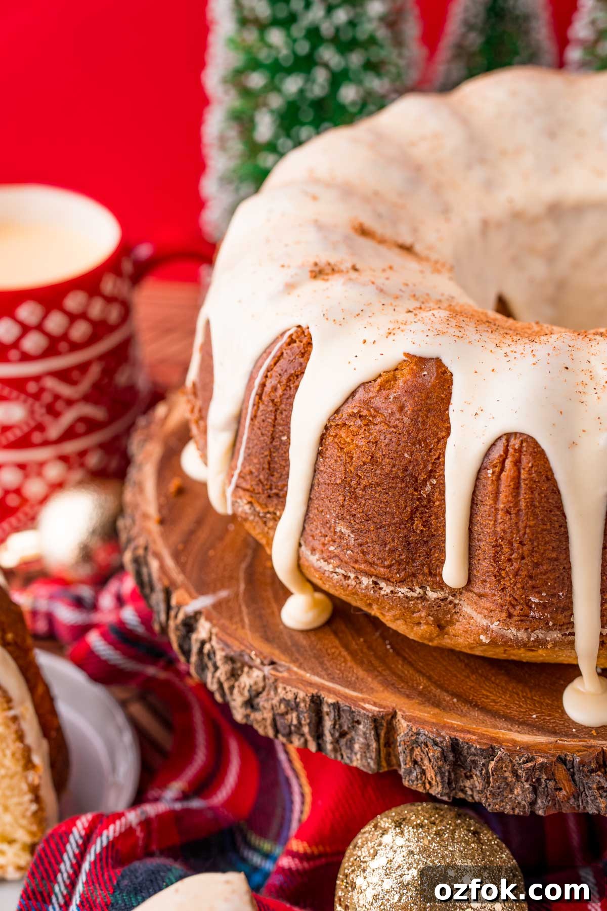 Close up photo of an eggnog pound cake on a wooden cake stand with holiday decorations in the background.