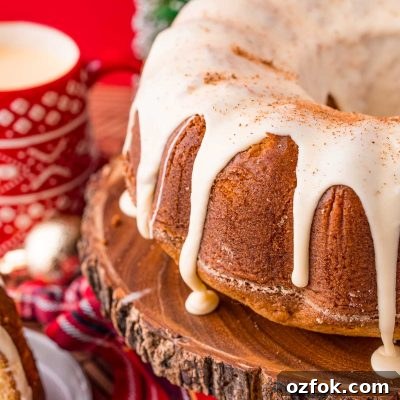 Close up photo of an eggnog pound cake on a wooden cake stand with holiday decorations in the background.