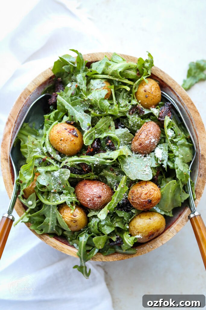 cooked potatoes with sun dried tomatoes and arugula in bowl with serving utensils