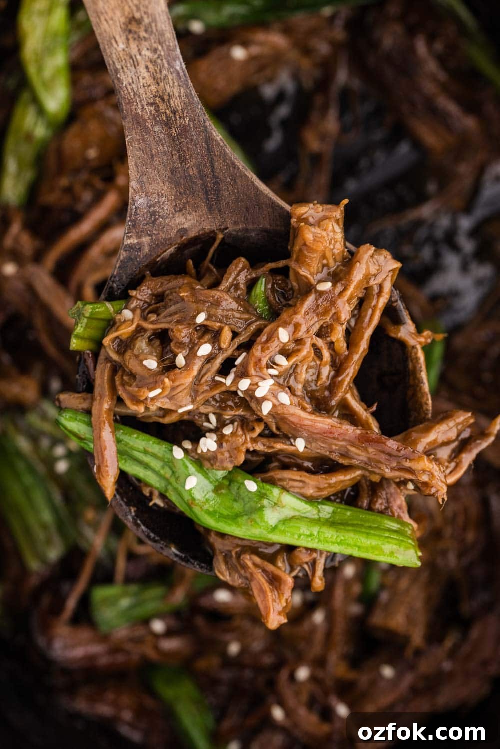 Close-up of a fork lifting tender shredded Mongolian beef, garnished with freshly sliced green onions