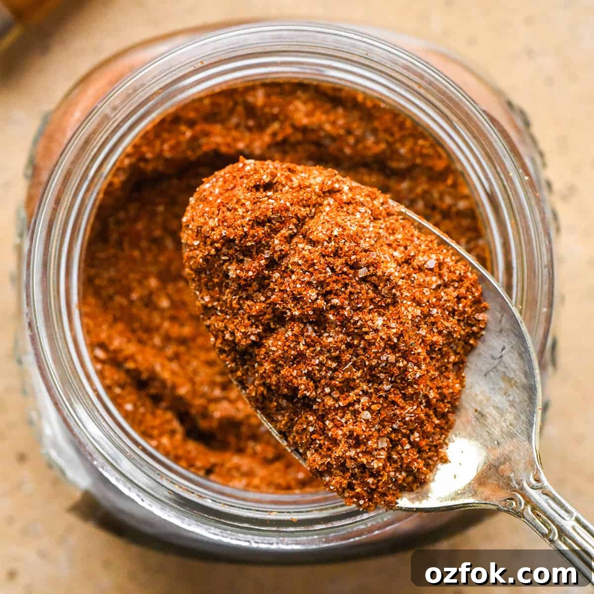 Homemade Chili Seasoning Blend for Bold, Authentic Flavor 13 up close overhead photo of a spoon taking a scoop of chili seasoning out of a glass jar