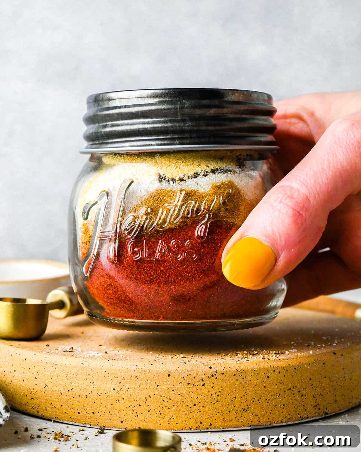 Homemade Chili Seasoning Blend for Bold, Authentic Flavor 7 a hand holding a glass jar with chili seasoning ingredients inside and a lid on before shaking