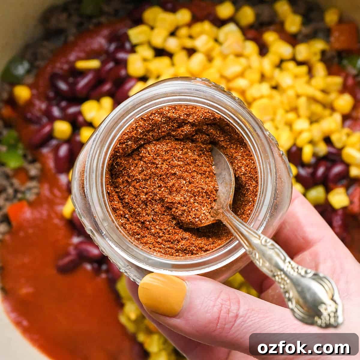 Homemade Chili Seasoning Blend for Bold, Authentic Flavor 10 Homemade Chili Seasoning in a glass jar being held over a pot of chili before adding.