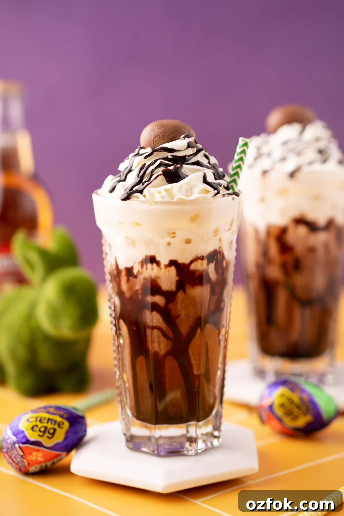 Crème Egg Dirty Soda Recipe: Candy-Inspired Creamy Fizzy Drink 2 A Cadbury Creme Egg flavored dirty soda on a white coaster on a yellow table.