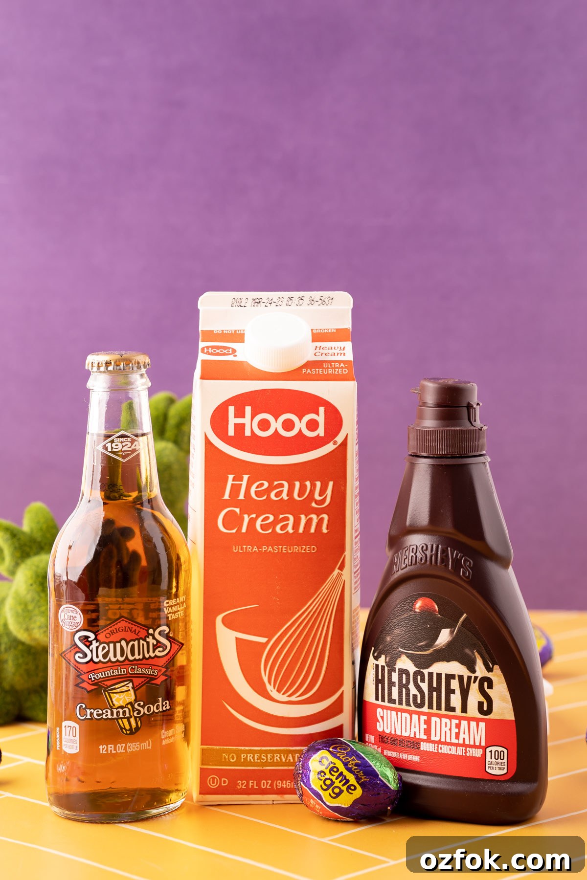 Crème Egg Dirty Soda Recipe: Candy-Inspired Creamy Fizzy Drink 4 Ingredients to make Cadbury Creme Egg Dirty Soda on a yellow table.