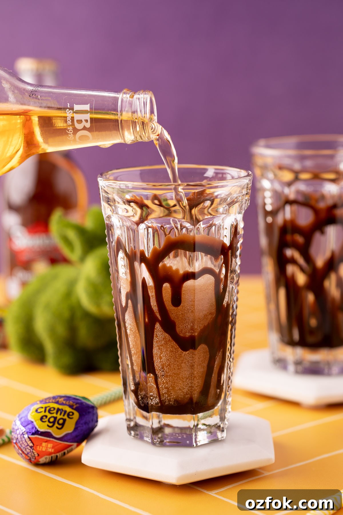 Crème Egg Dirty Soda Recipe: Candy-Inspired Creamy Fizzy Drink 5 Cream soda being poured into a glass with chocolate syrup.