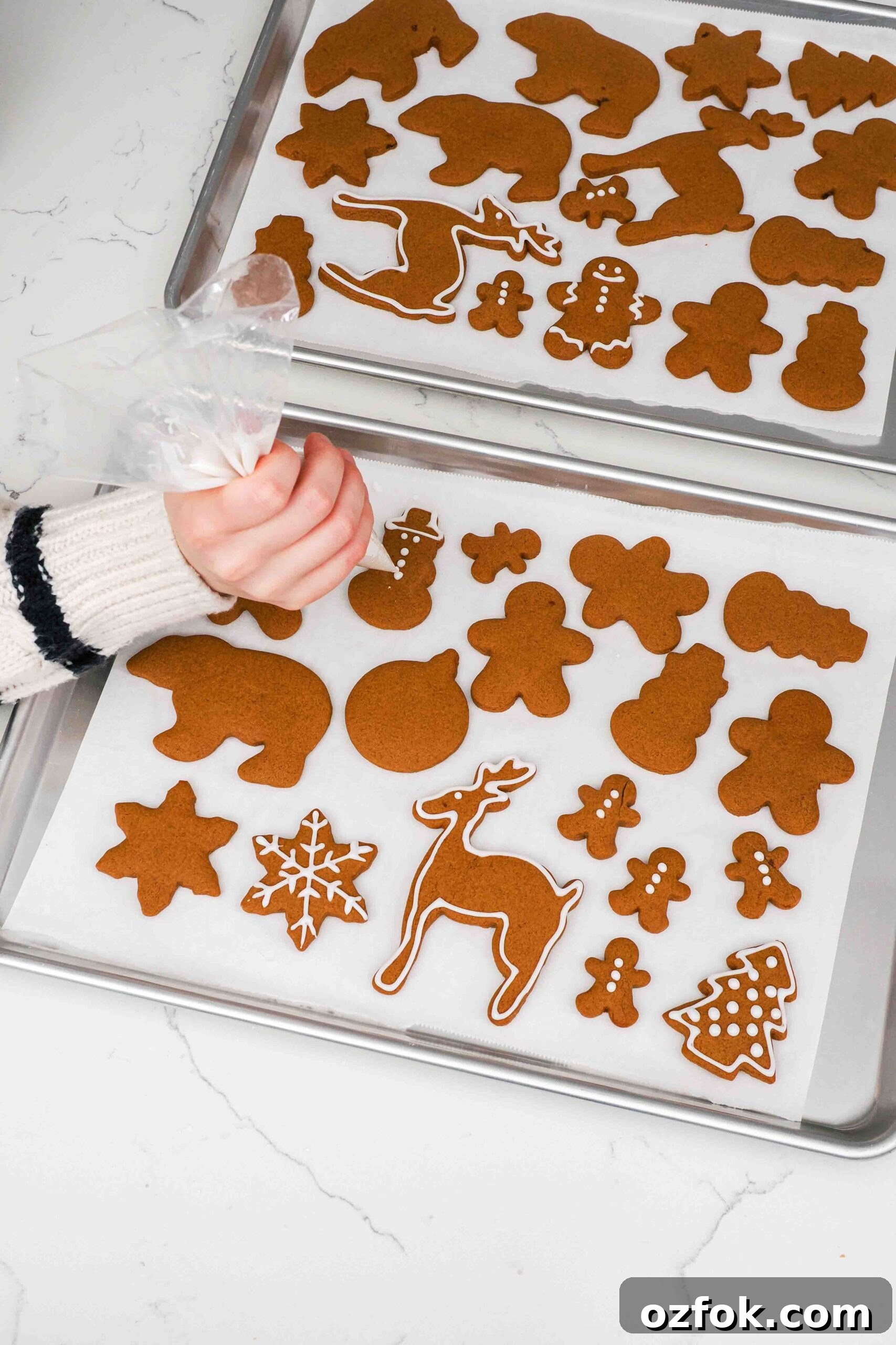 A hand pipes icing onto gingerbread cookies.
