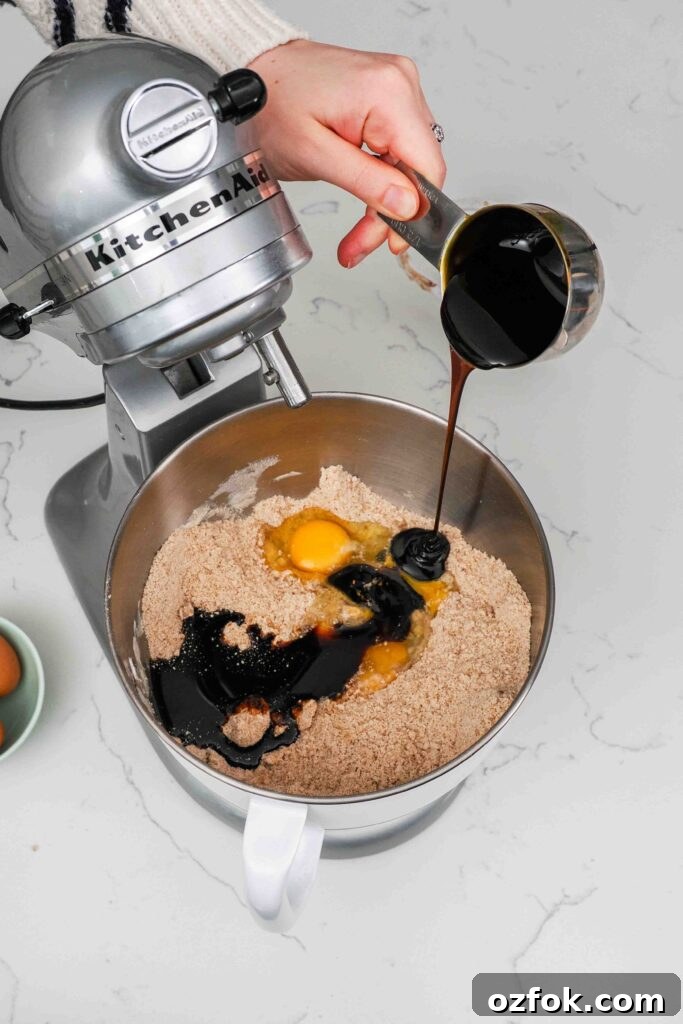 Eggs and molasses are added to a mixer bowl with dry ingredients for gingerbread cookies.