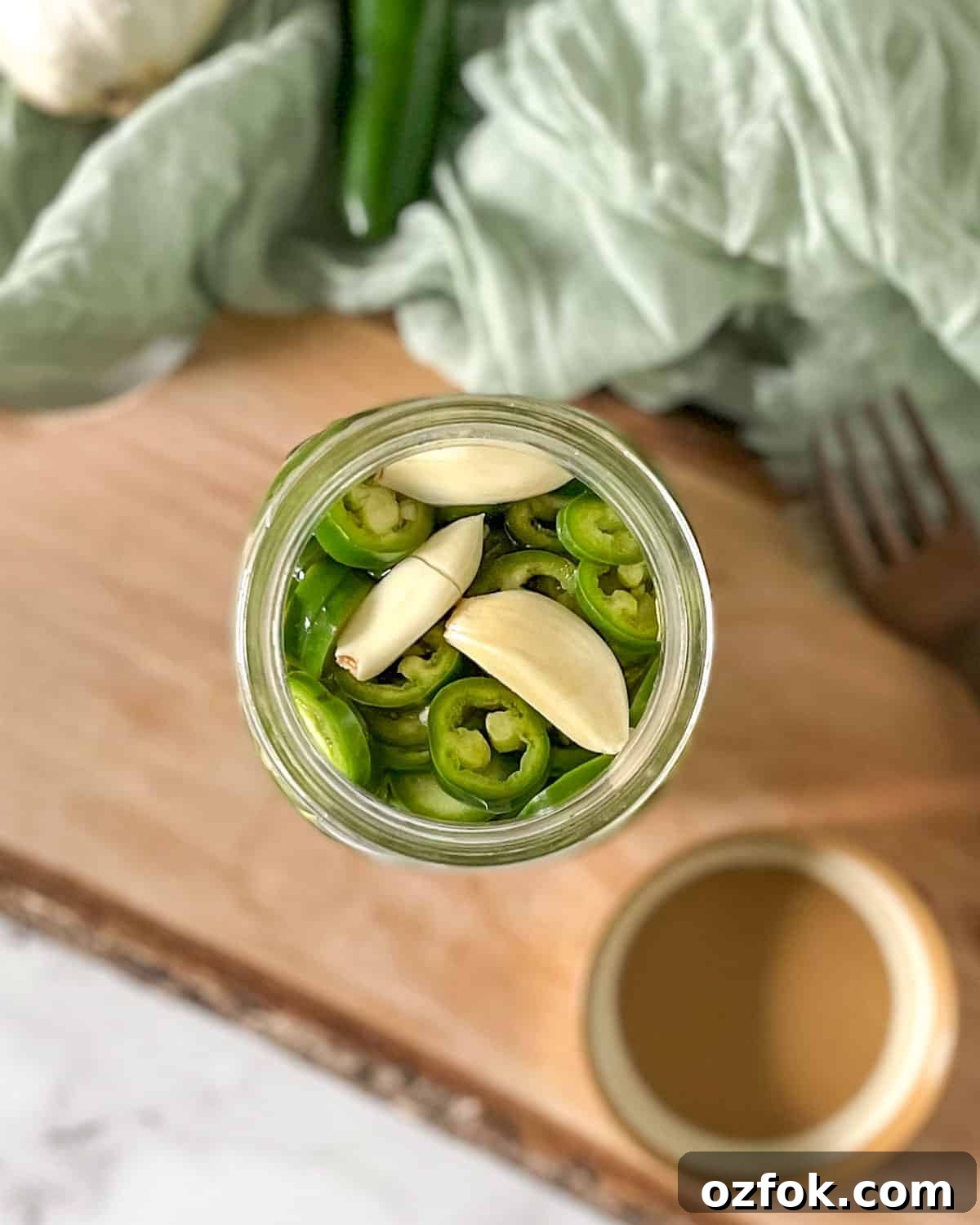 Quick Pickled Serrano Peppers Recipe for Tangy, Crisp Jalapeño-Style Peppers 2 Pickled serrano peppers are shown in a glass jar surrounded by garlic, serrano peppers, and a fork.