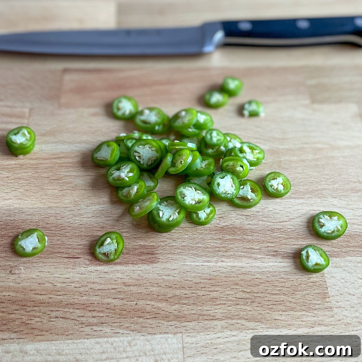 Quick Pickled Serrano Peppers Recipe for Tangy, Crisp Jalapeño-Style Peppers 4 Sliced serrano peppers sit on a wooden cutting board with a kitchen knife in the background.