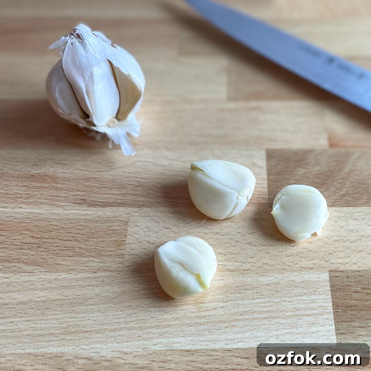 Quick Pickled Serrano Peppers Recipe for Tangy, Crisp Jalapeño-Style Peppers 5 Three cloves of smashed garlic sit in front of a partial head of garlic and a kitchen knife on a wooden cutting board.