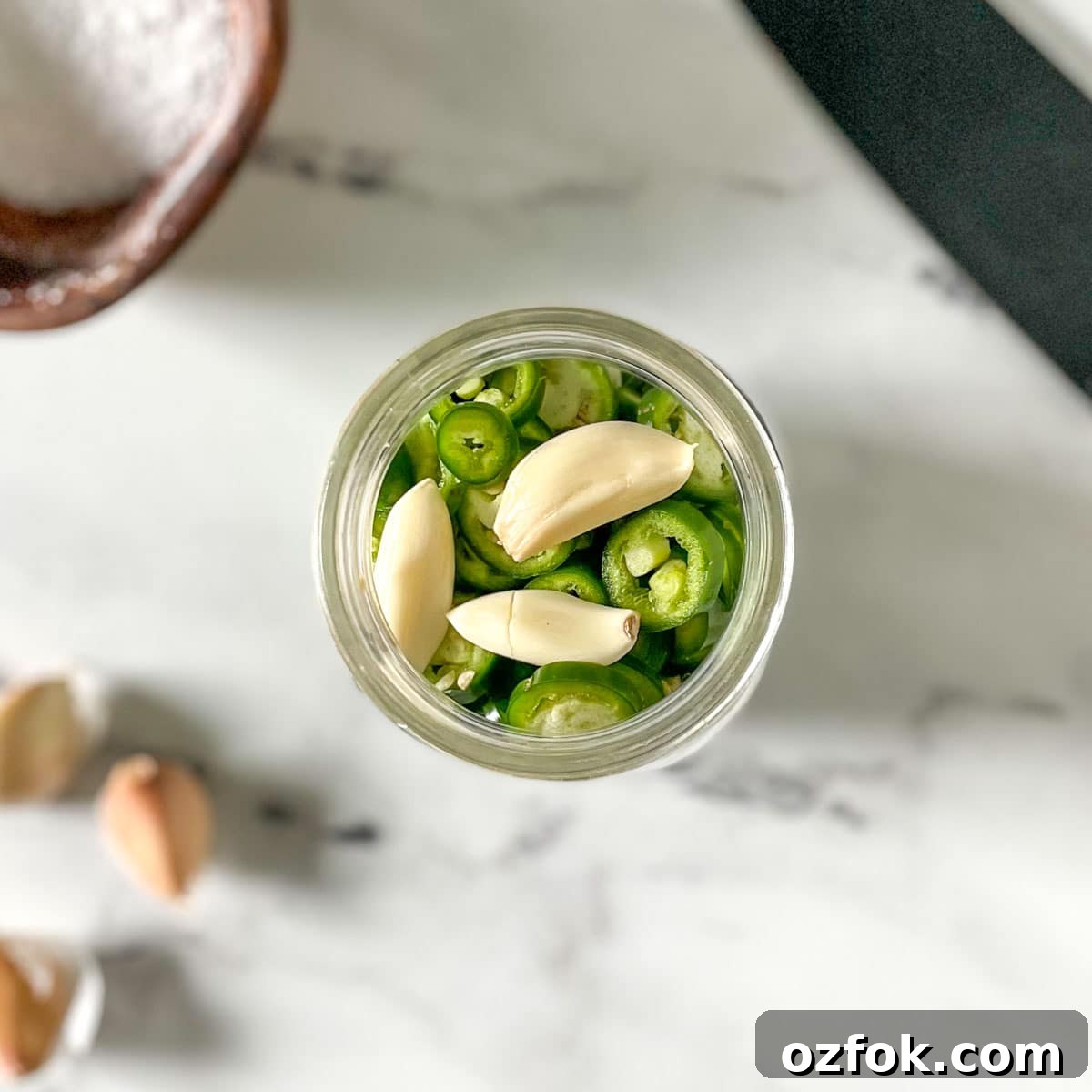 Quick Pickled Serrano Peppers Recipe for Tangy, Crisp Jalapeño-Style Peppers 6 Sliced serrano peppers and smashed garlic cloves are shown in a glass jar.