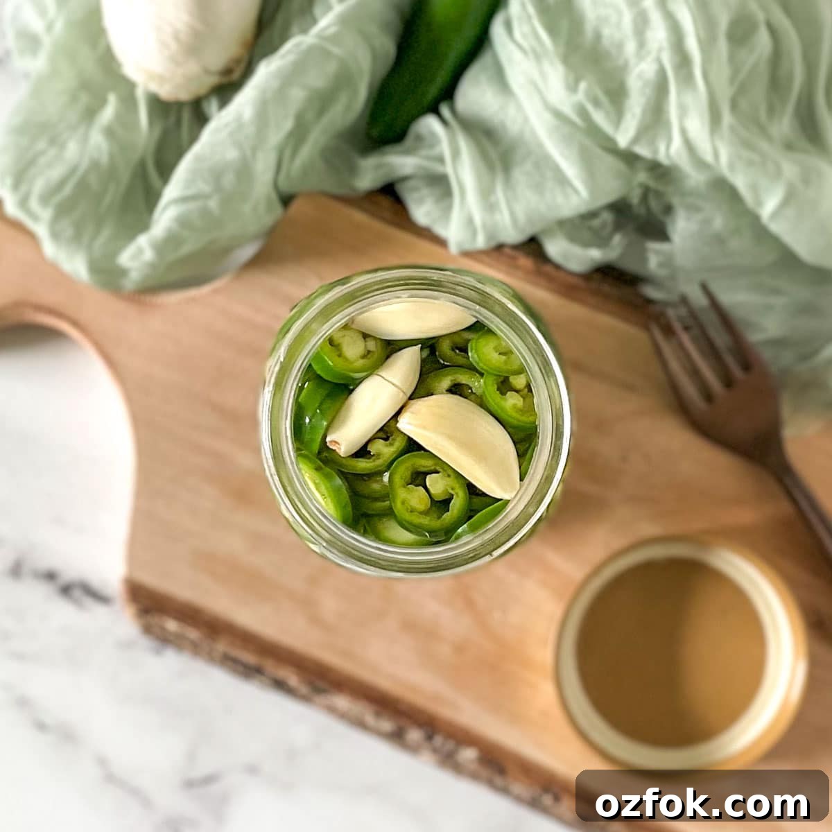 Quick Pickled Serrano Peppers Recipe for Tangy, Crisp Jalapeño-Style Peppers 8 Pickled serrano peppers are shown in a glass jar surrounded by garlic, serrano peppers, and a fork.
