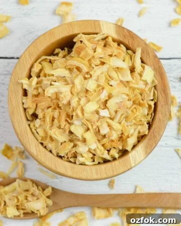 Overhead photo of a small wooden bowl and spoon filled with dehydrated onion flakes.