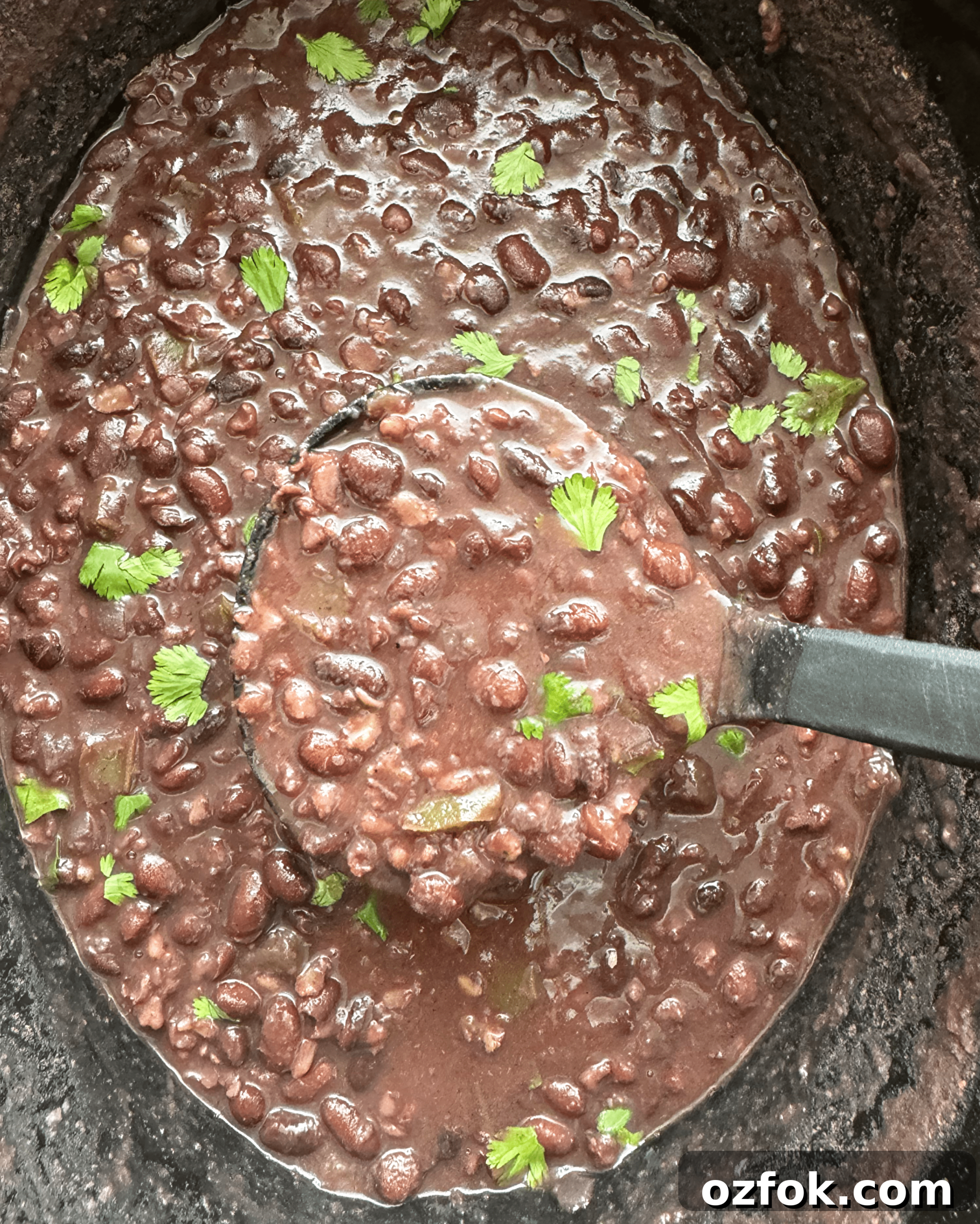 overhead shot of cooked mexican black beans and rice in a black slow cooker garnished with fresh cilantro