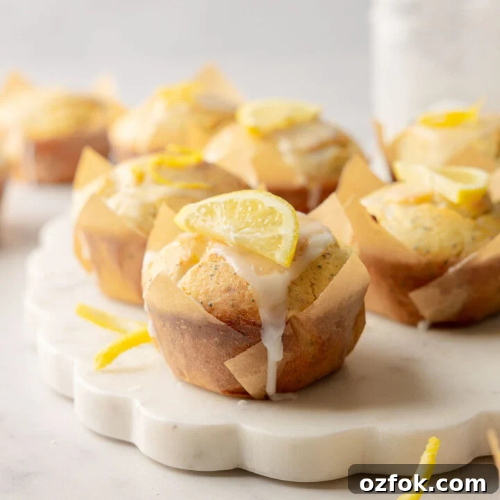 Lemon poppy seed muffins with glaze and lemon slice garnish on marble board.
