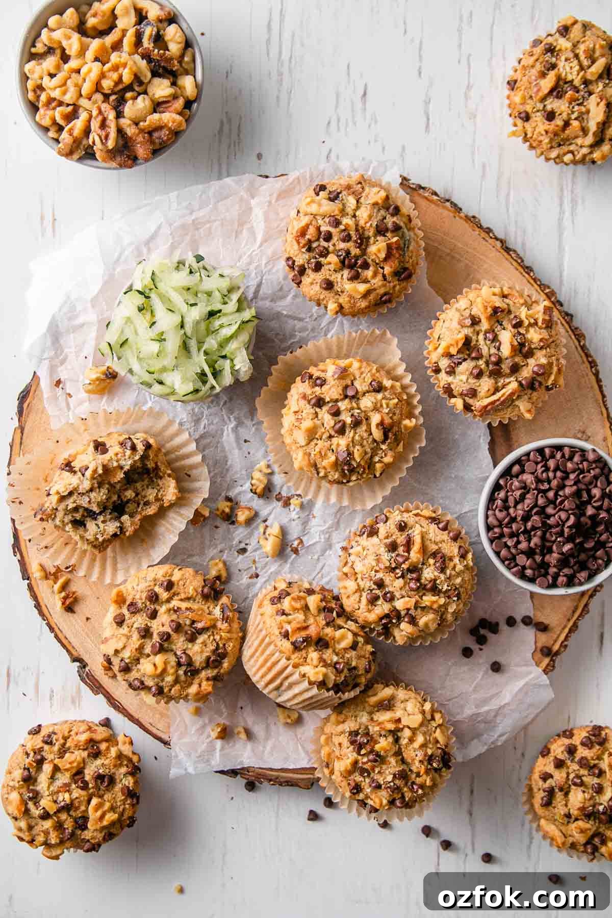 Gluten-Free Dairy-Free Zucchini Muffins Recipe 6 Gluten-free zucchini muffins on a round wood slice platter next to shredded zucchini and a bowl of chocolate chips.