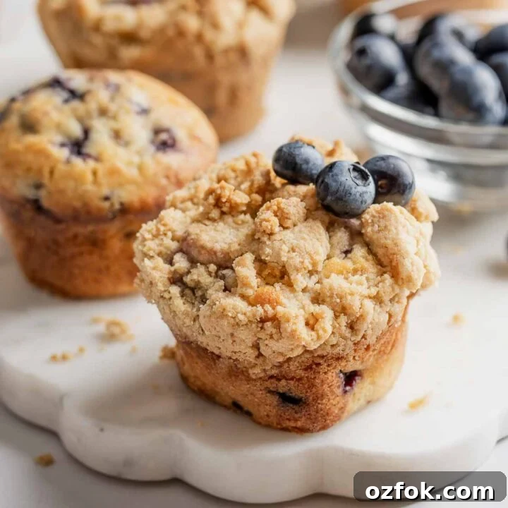 Gluten-free blueberry muffins with streusel and garnished with fresh blueberries, on marble platter.