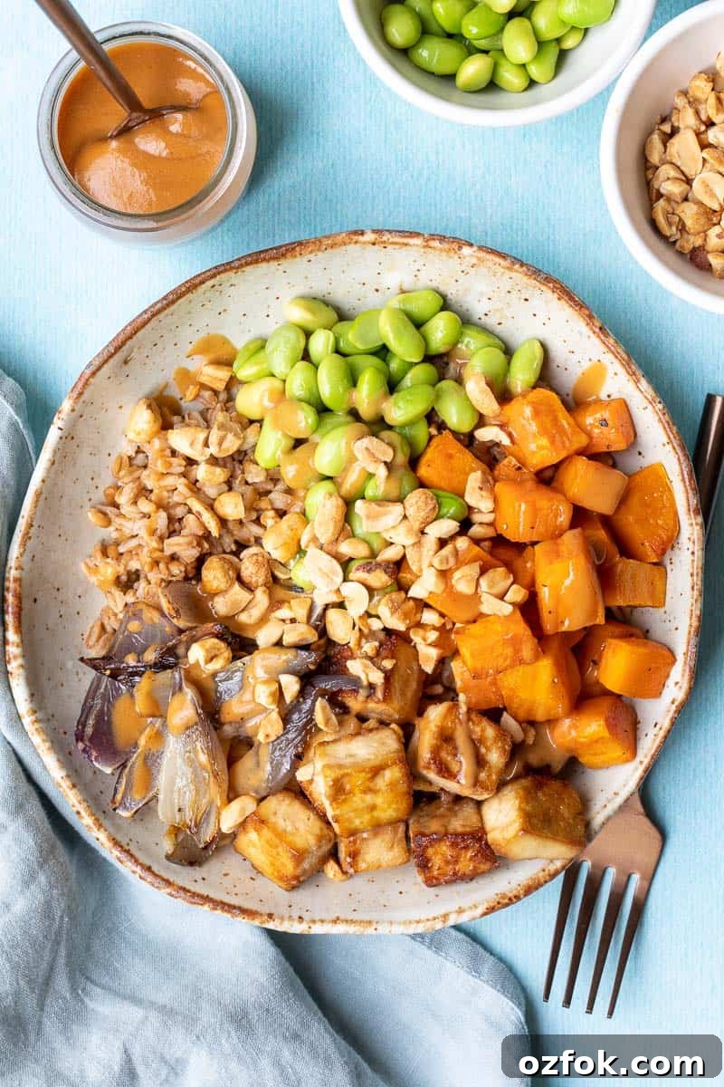 Crispy Tofu Buddha Bowl with Sesame Ginger Dressing 2 overhead shot of tofu buddha bowl with peanut sauce next to fork, napkin, and bowls of peanut sauce, edamame, and chopped peanuts.