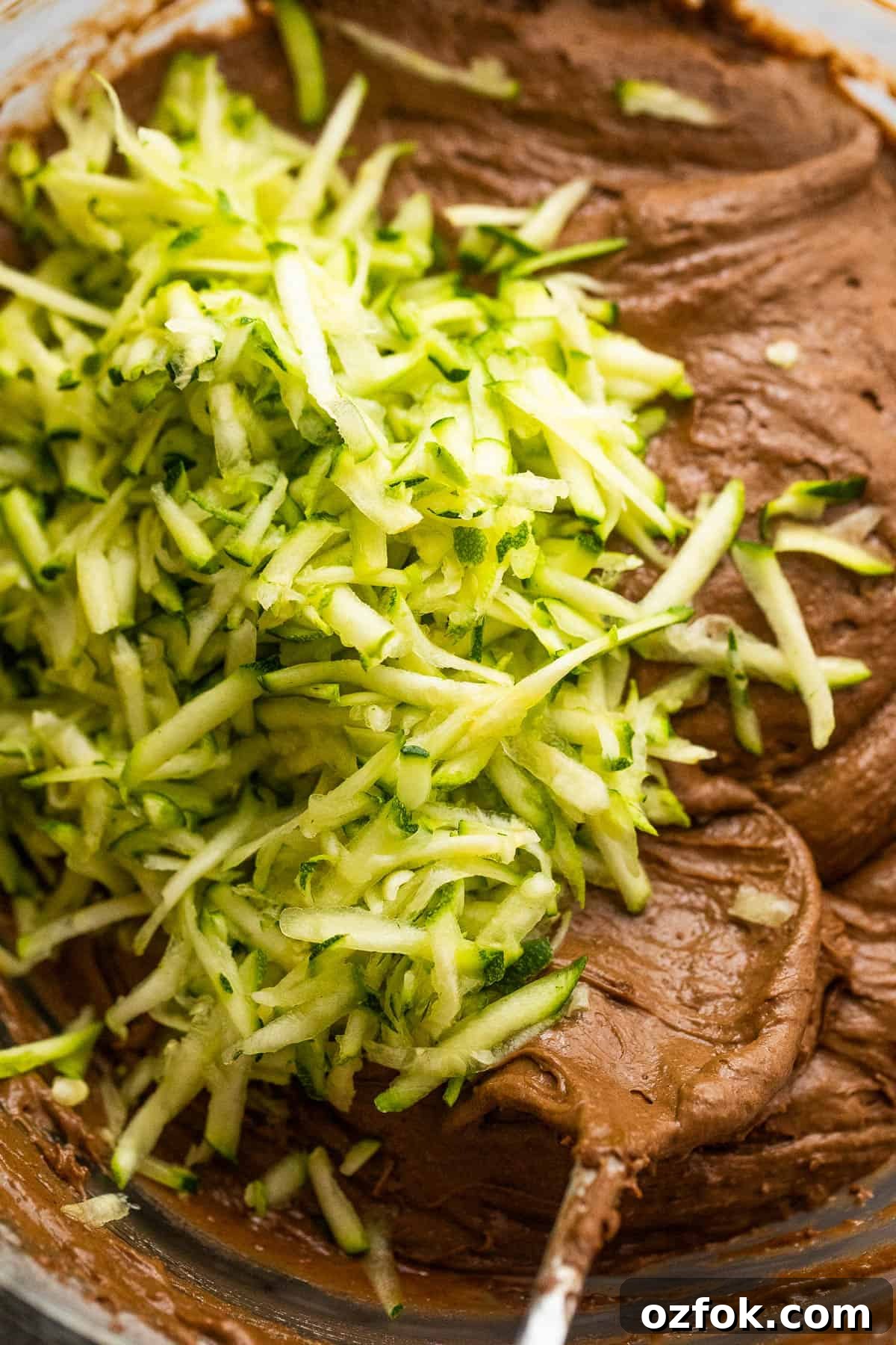 mixing shredded zucchini into a chocolate batter for zucchini bread