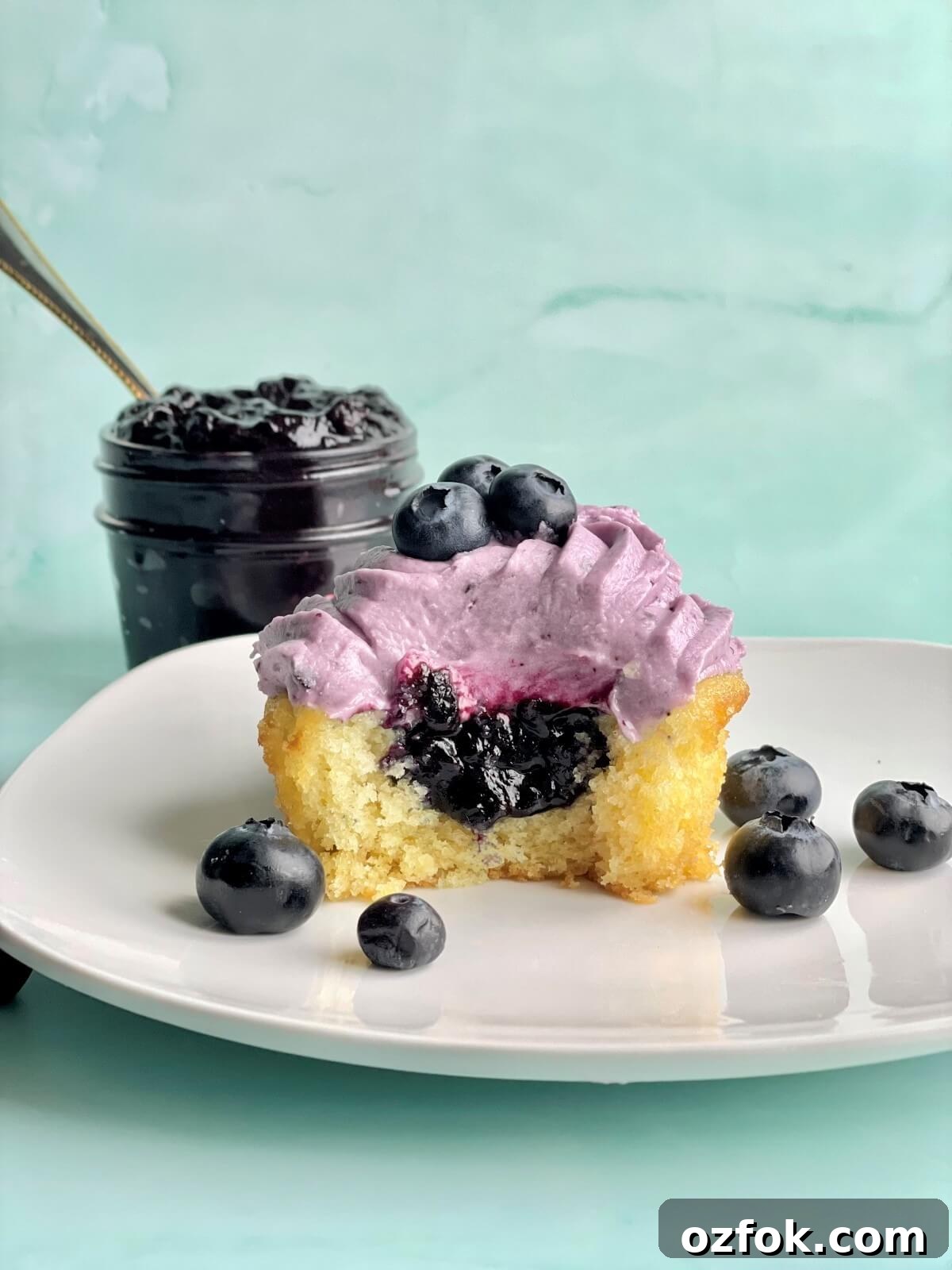 a vanilla cupcake with blueberry cupcake filling and a bowl of blueberry compote filling in the background