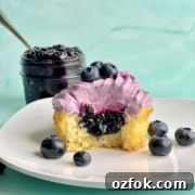 a vanilla cupcake with blueberry cupcake filling and a bowl of blueberry compote filling in the background