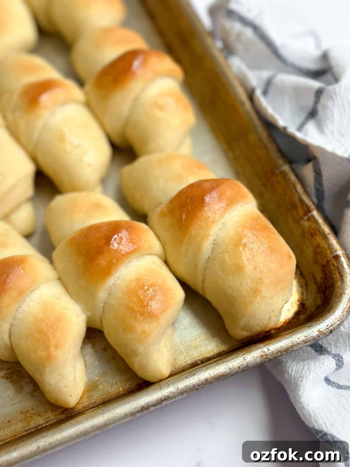 Flaky Homemade Buttery Dinner Rolls Recipe 2 a closeup up of buttery homemade crescent rolls on a baking sheet.