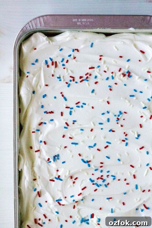 Patriotic Red White & Blue Poke Cake Recipe for 4th of July 4 the top (overhead view) of a patriotic poke cake, with whipped cream and red, white, and blue sprinkles