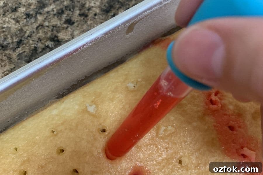 Patriotic Red White & Blue Poke Cake Recipe for 4th of July 7 a hand adding red jello to the holes of the poke cake, using a dropper