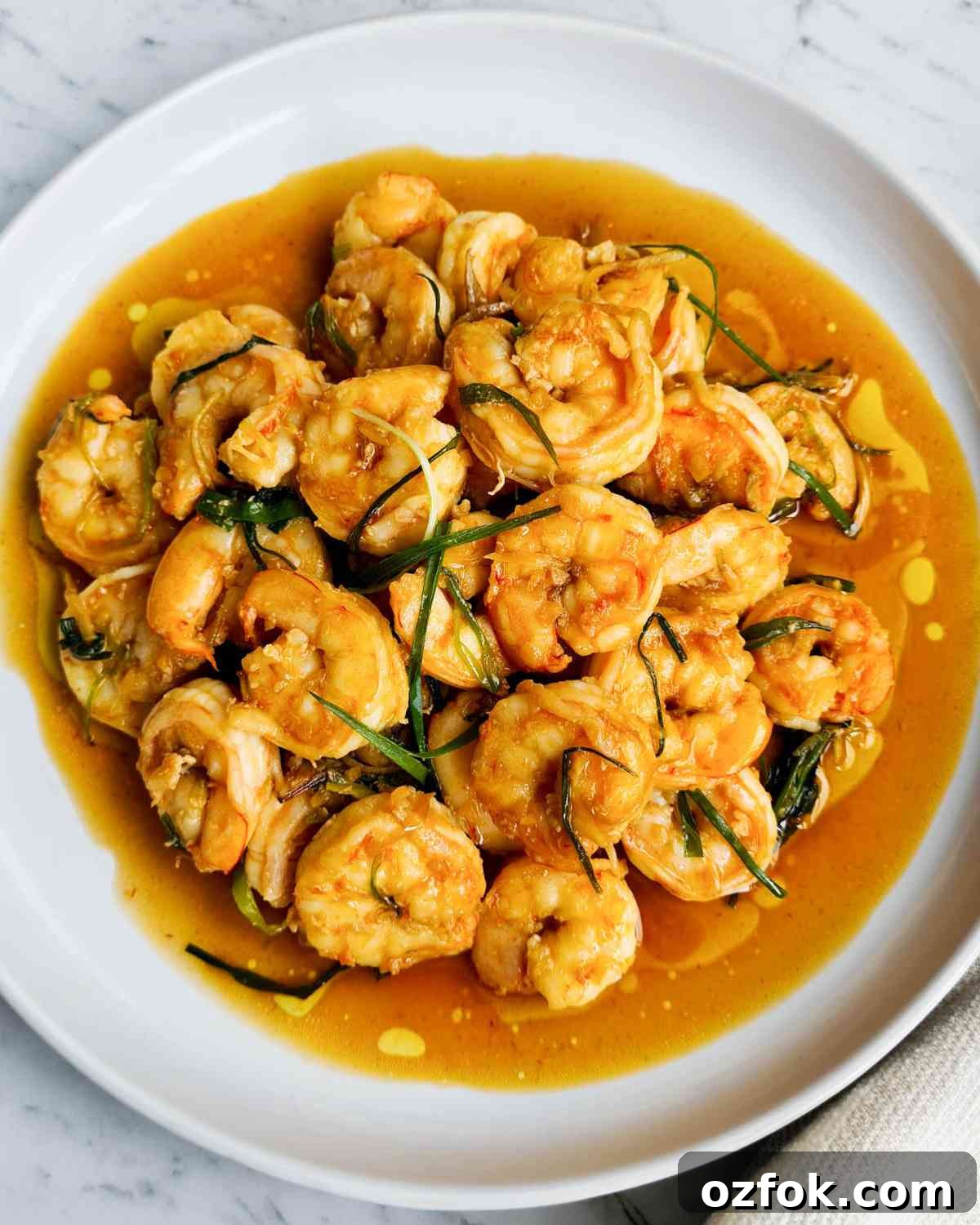 Chinese-Style Prawn Stir-Fry with Ginger and Spring Onions 2 Cooked peeled prawns on a white plate with sauce