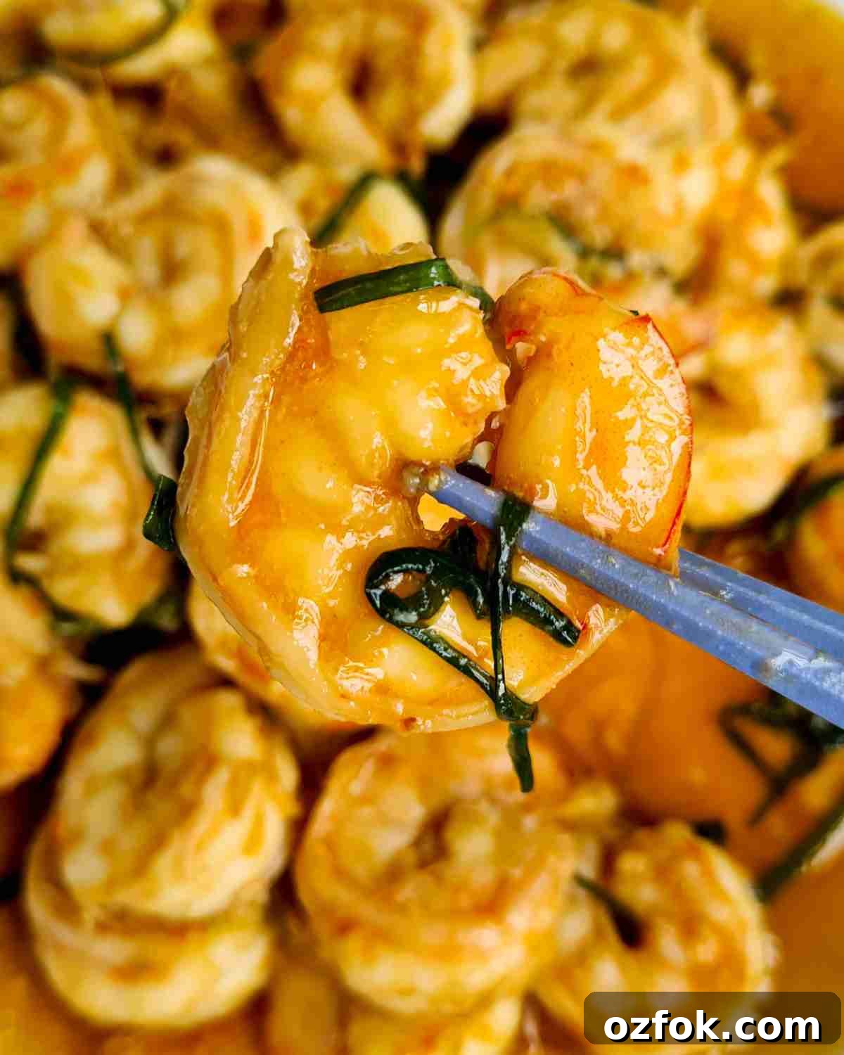 Chinese-Style Prawn Stir-Fry with Ginger and Spring Onions 11 Close up of a piece of cooked peeled prawn held up by a pair of chopsticks