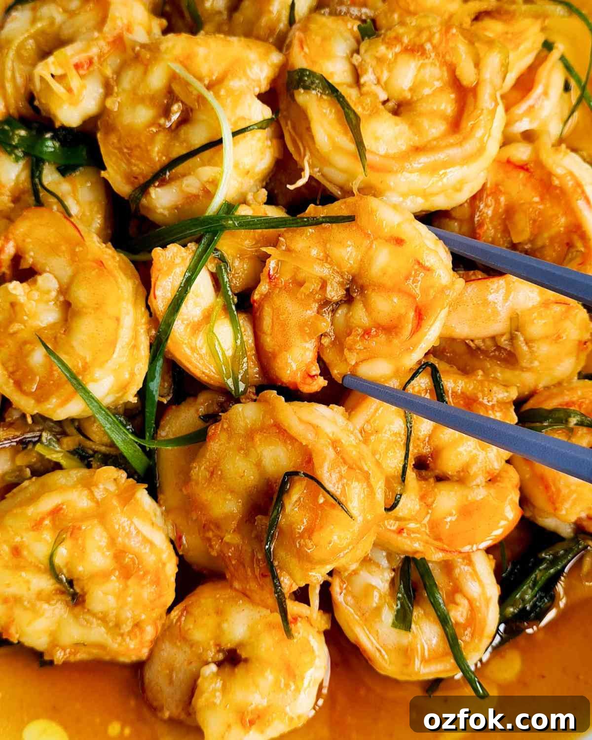 Chinese-Style Prawn Stir-Fry with Ginger and Spring Onions 13 Close up of stir fried prawns in sauce with a piece being held up by a pair of chopsticks
