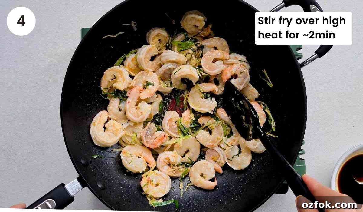 Chinese-Style Prawn Stir-Fry with Ginger and Spring Onions 8 peeled prawns being stir fried in a large wok with caption