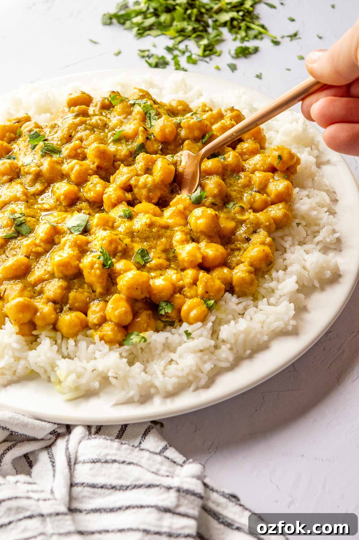 Quick and Flavorful Pea Curry Recipe for Weeknight Meals 6 Hand taking a spoonful of chickpeas in creamy yellow sauce on a white plate.