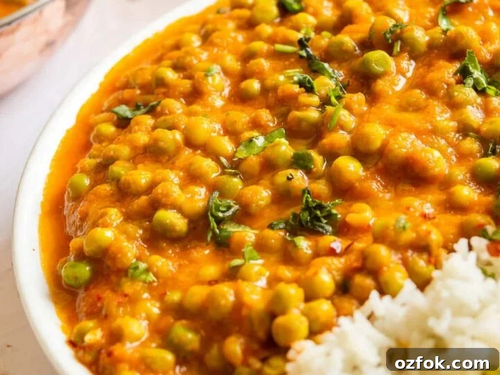 Front view of a plate with a little white rice and lots of peas in orange sauce.
