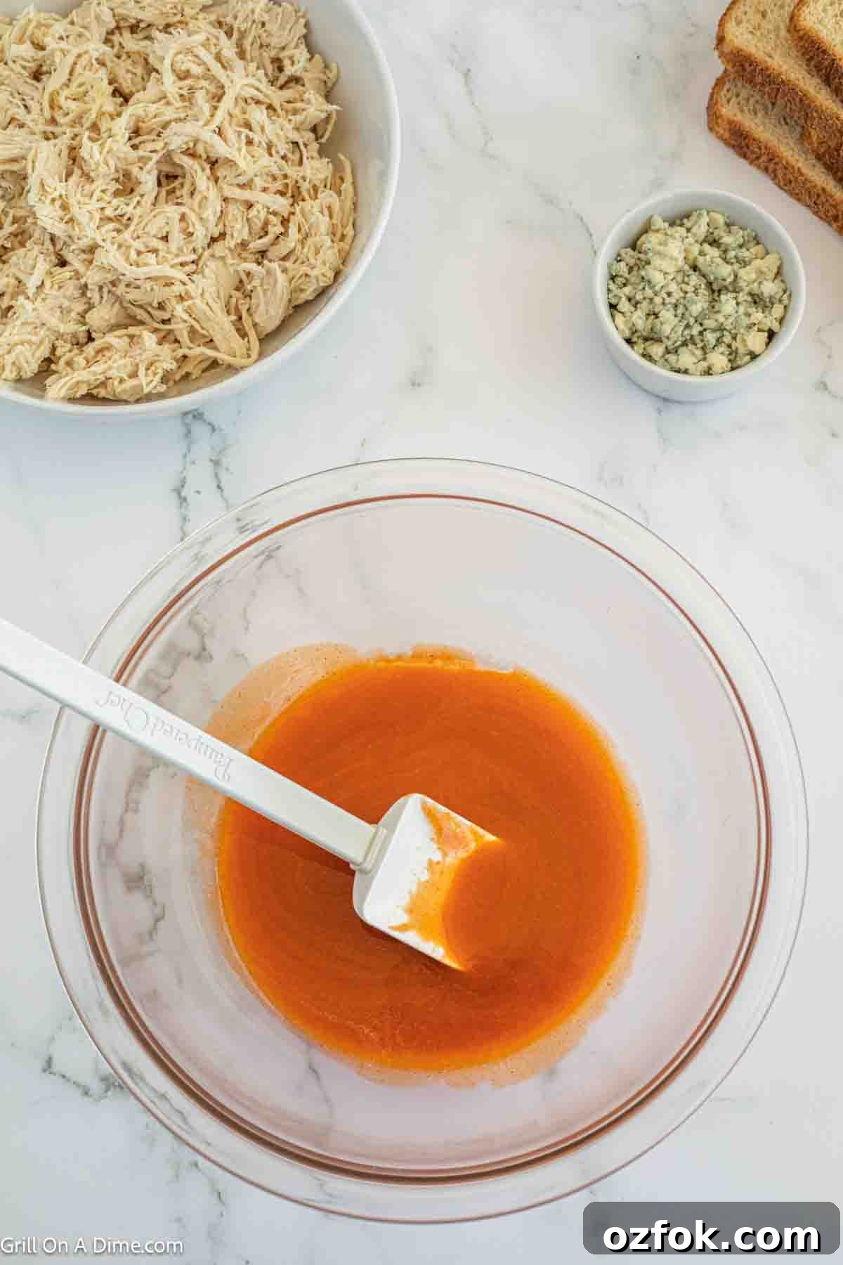Buffalo sauce mixed with melted butter in a bowl with a spatula