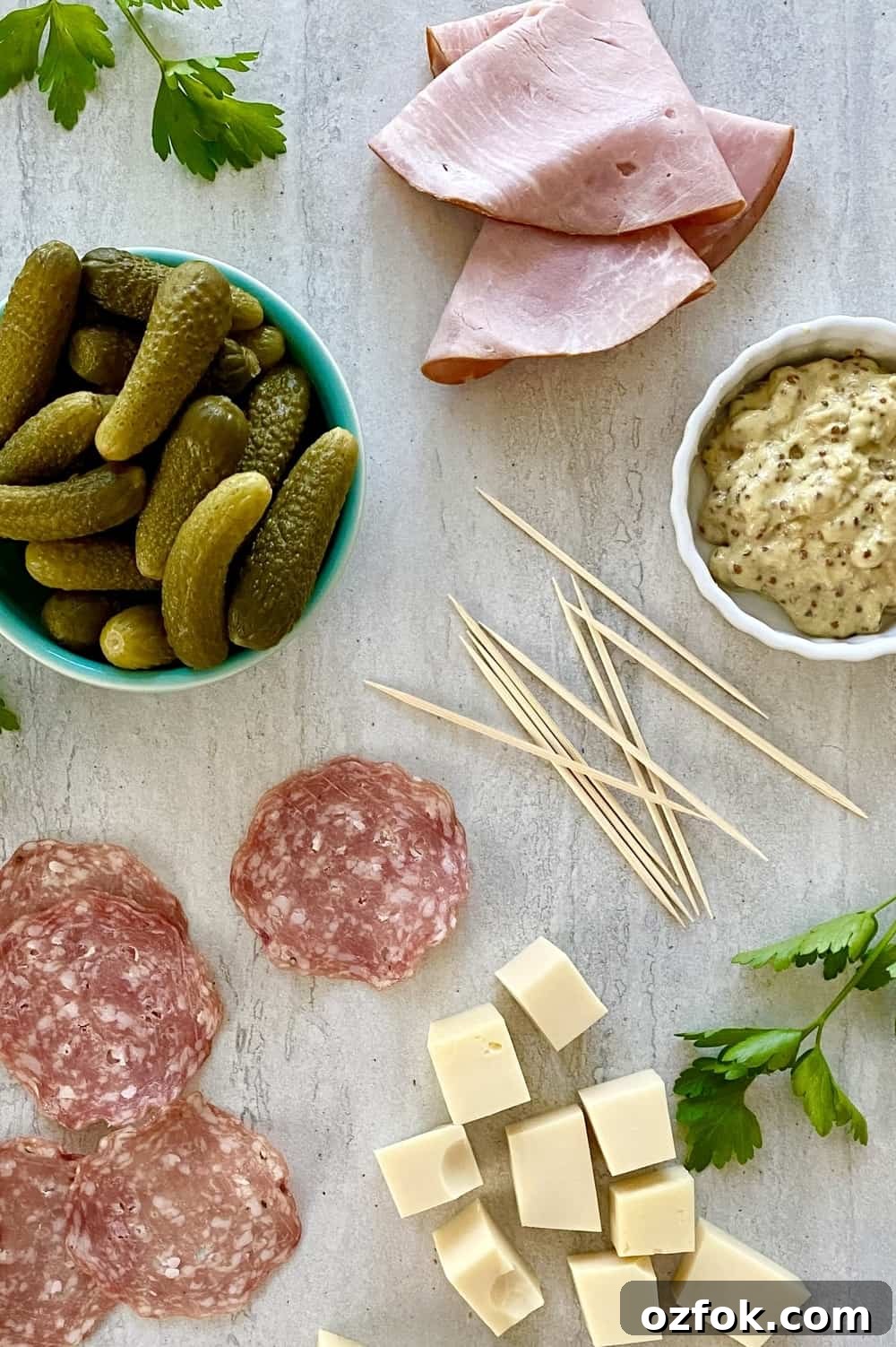 Ham slices, Swiss cheese, salami, dill pickles, mustard on a marble counter.