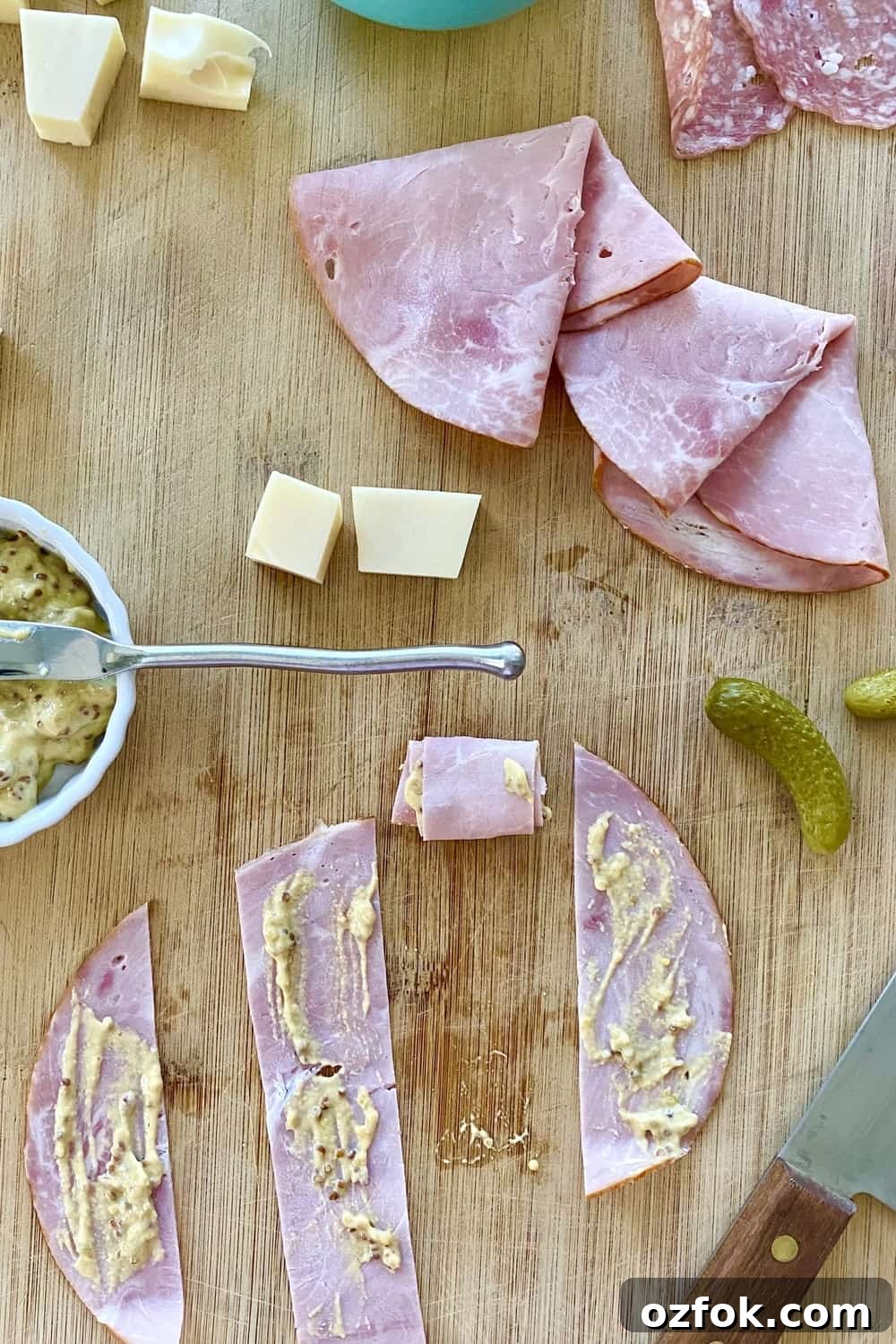 Strips of ham spread with mustard with small pickles and cheese cubes.