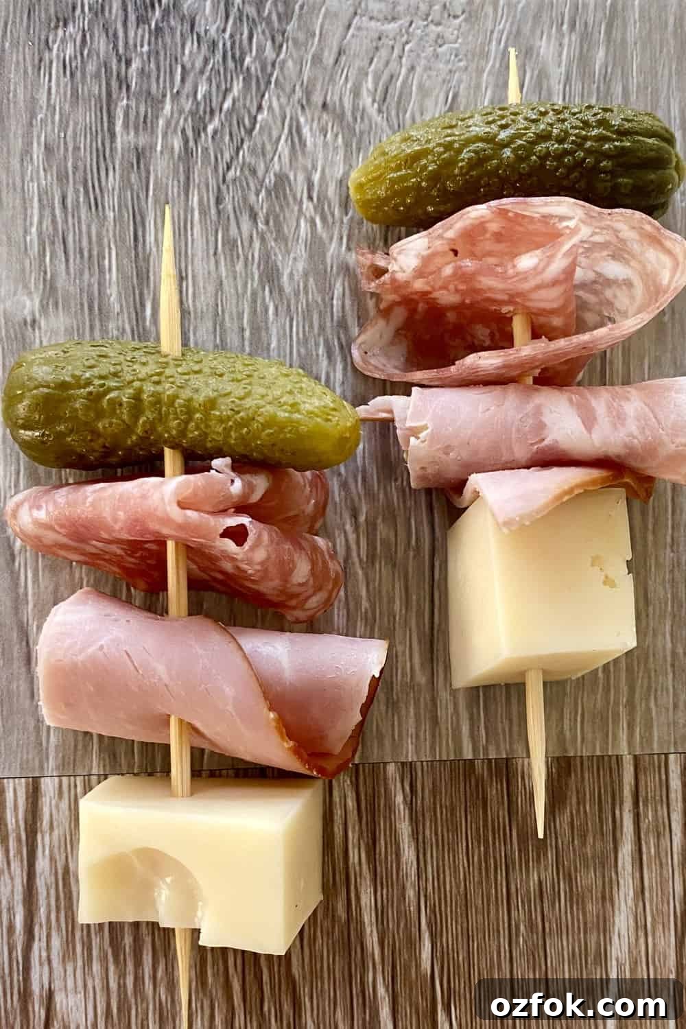 A toothpick with a cheese cube, ham roll up, salami roll up and a small pickle.