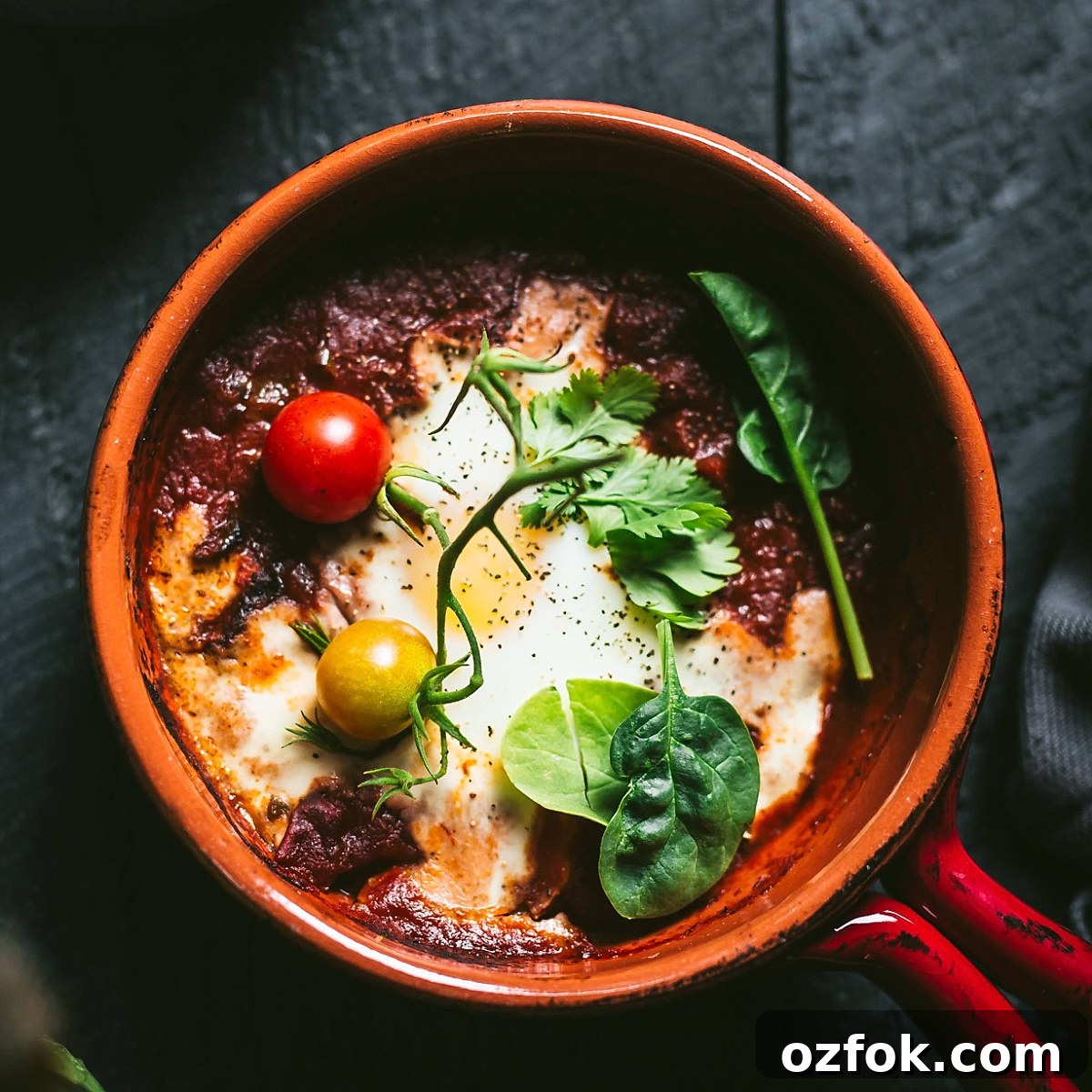 shakshuka for one in a small crock garnished with cherry tomatoes, spinach, cilantro