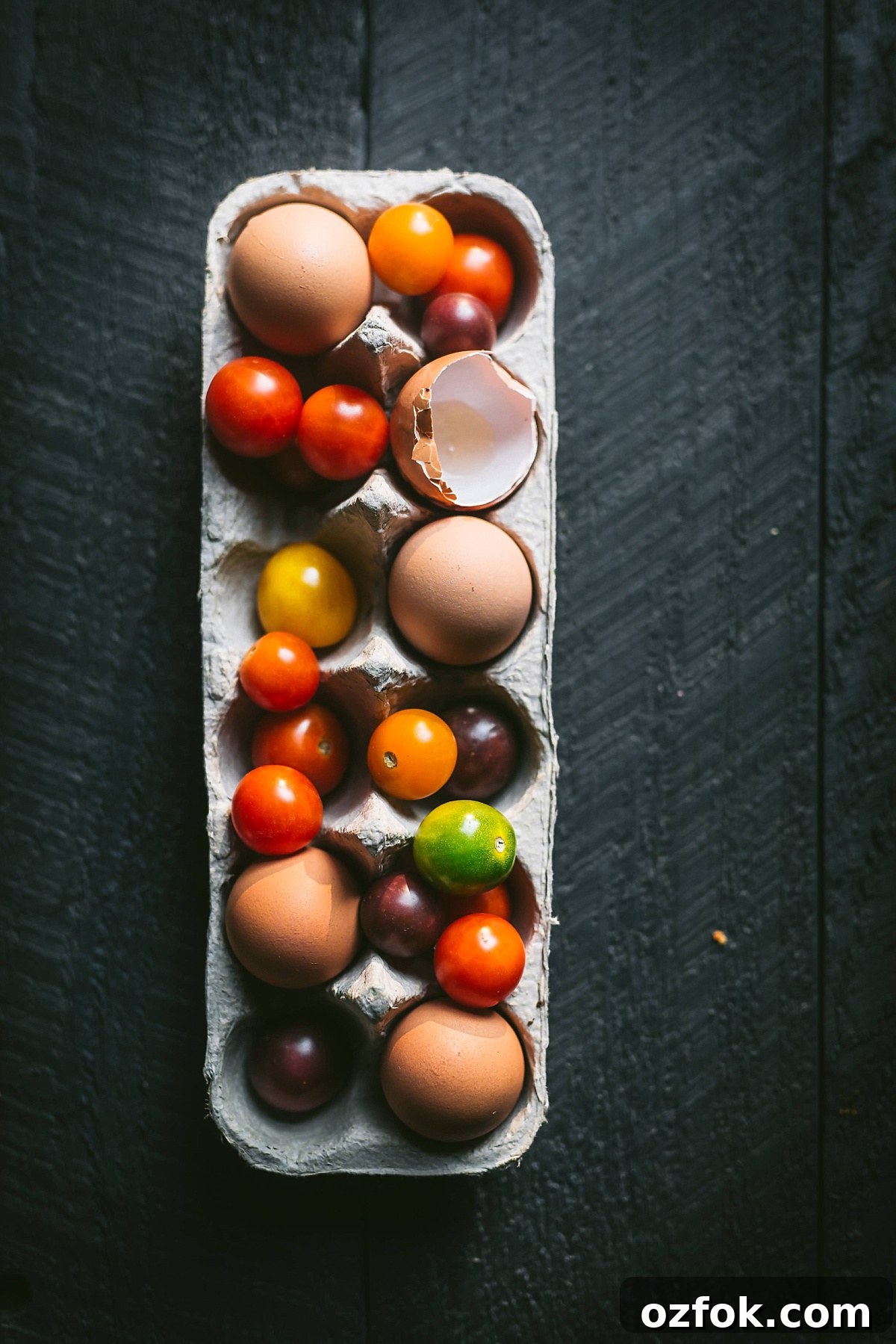egg carton full of brown eggs, multicolored heirloom tomatoes, and cracked/empty eggshells