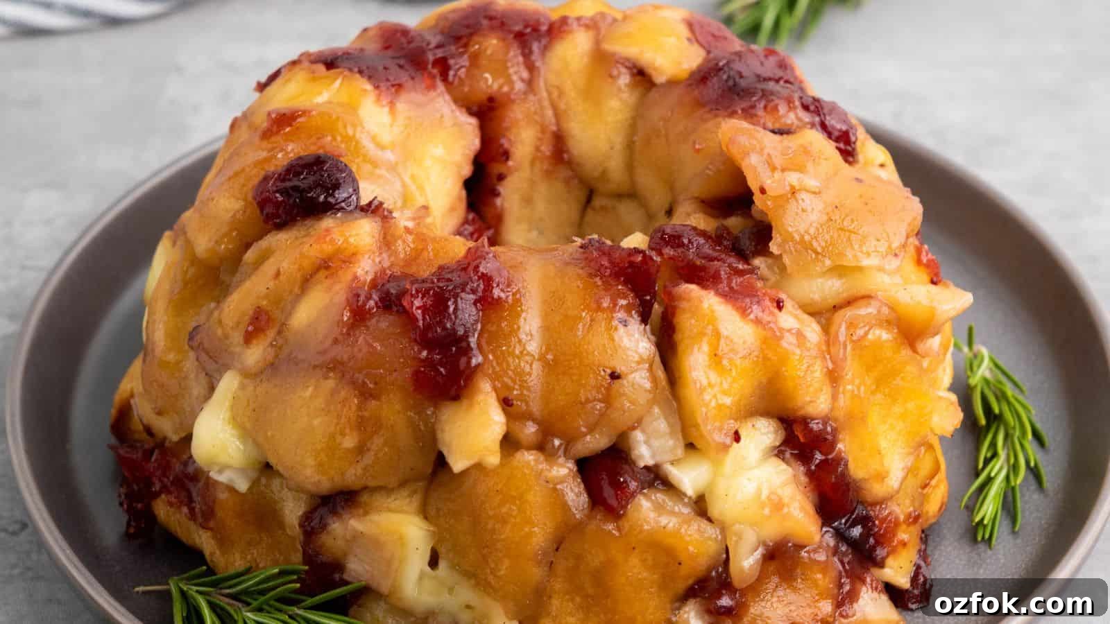 A baked pull-apart bread ring with melted cheese and cranberries on a gray plate, garnished with rosemary sprigs.