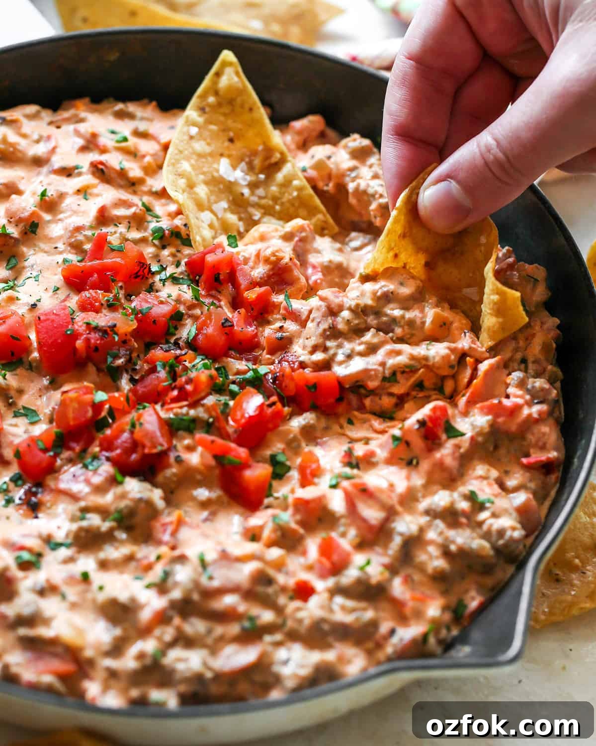 front view of a chip being dipped into a skillet of Cream Cheese Sausage Dip