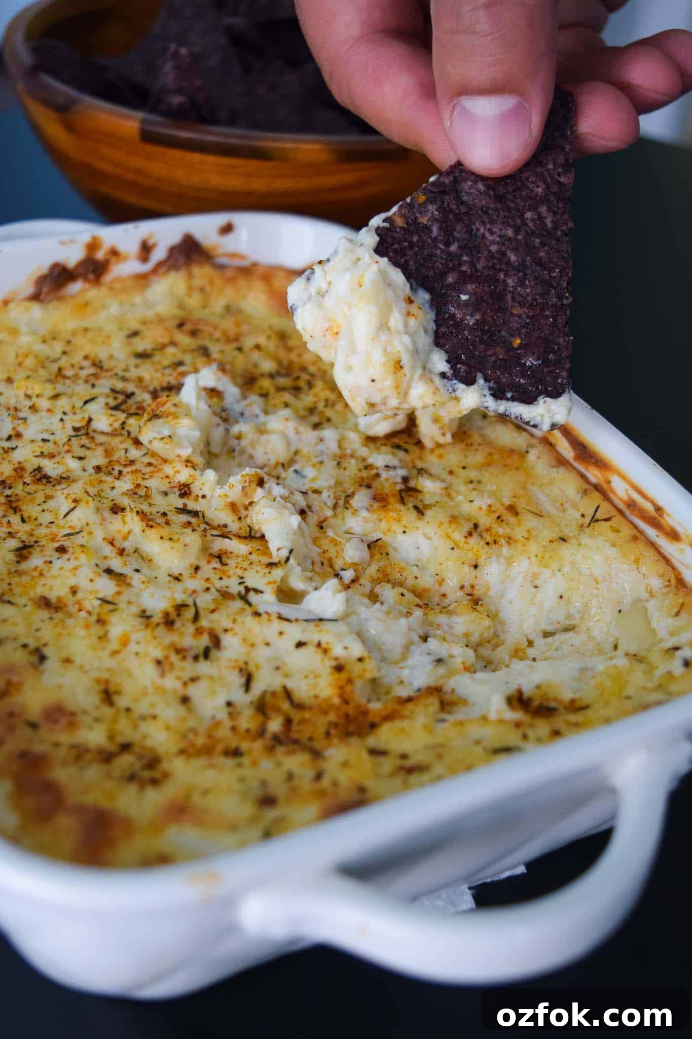 White Cheddar Onion Dip in white platter with chip being dipped into it